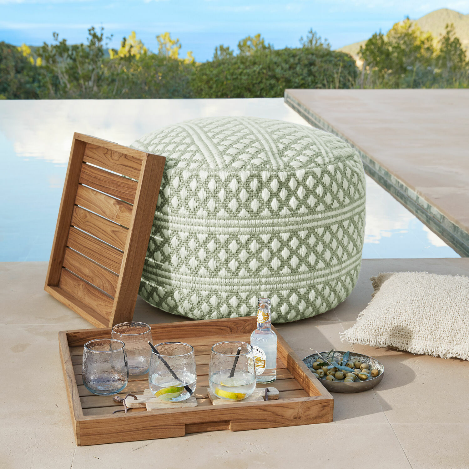 Taburete para interior y exterior Mintares Puf suave verde y blanco de tela con patrón geométrico en terraza junto a la piscina