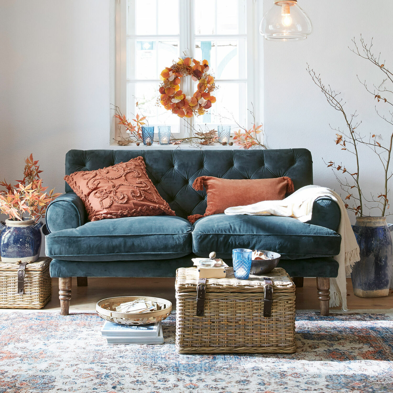 Sofá Carme Sofá de terciopelo azul oscuro con cojines color óxido y mesa de mimbre en sala acogedora