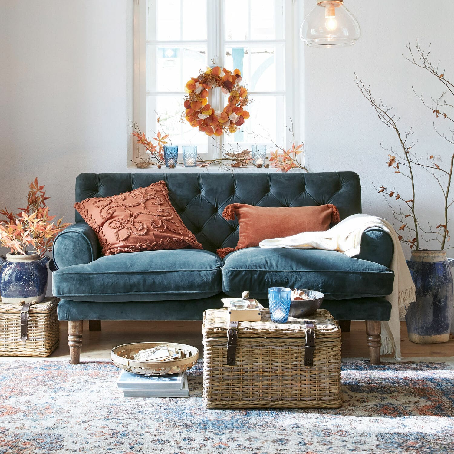 Sofá Carme Sofá de terciopelo azul oscuro con cojines color óxido y mesa de mimbre en sala acogedora