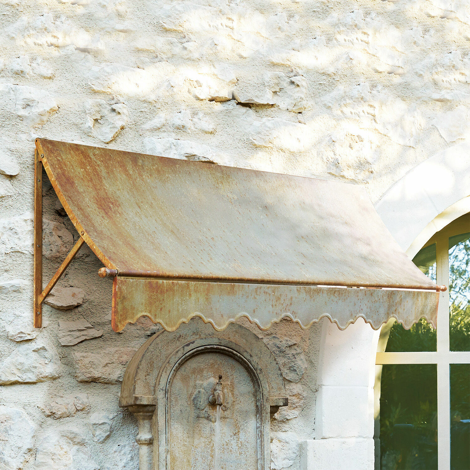 Marquesina Maltot Toldo metálico oxidado sobre pared de piedra con ventana y fuente antigua