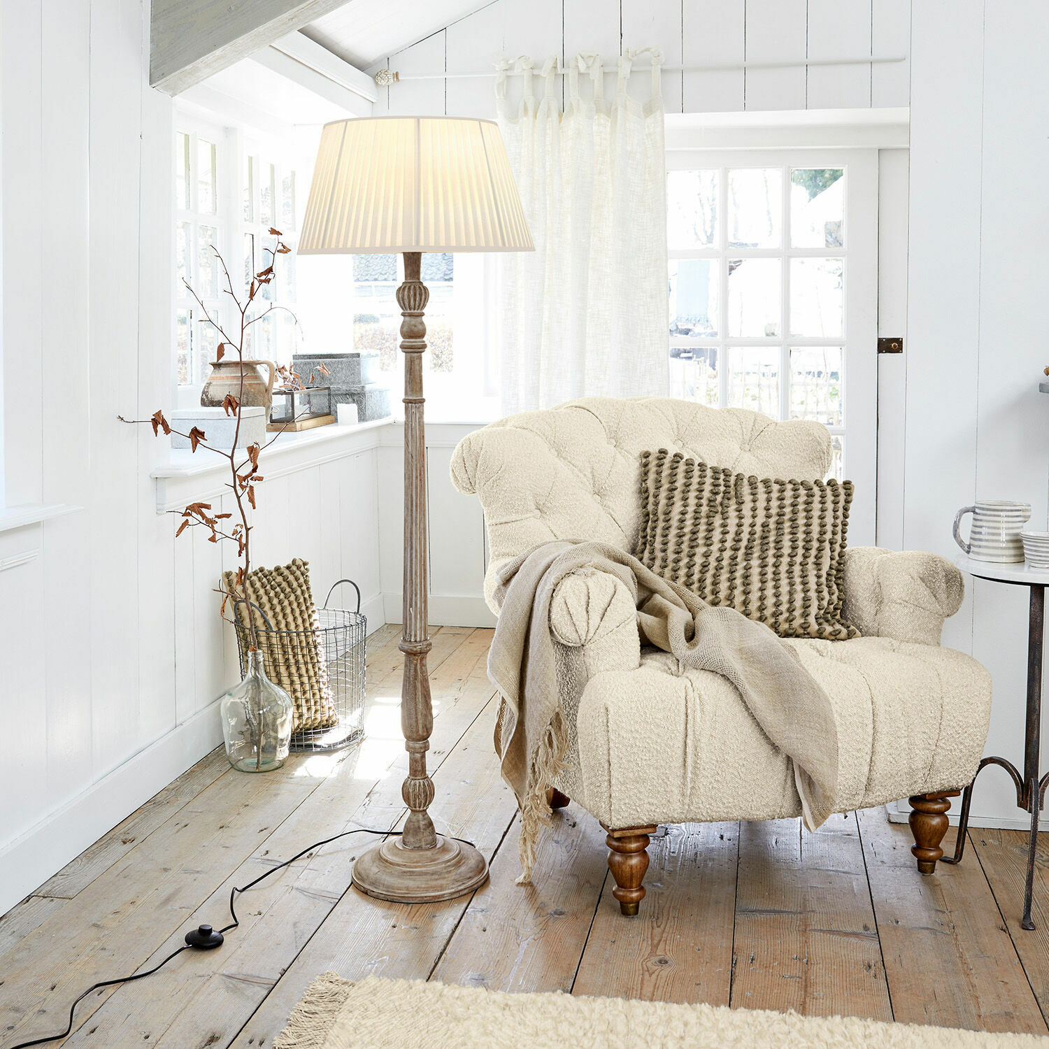 Lámpara de pie Morten Sillón beige de tela bouclé con cojín y lámpara de pie en sala luminosa de madera