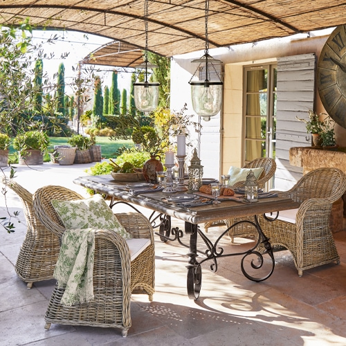 Conjunto de muebles de jardín de mimbre y metal en tonos naturales en terraza con decoraciones y lámparas