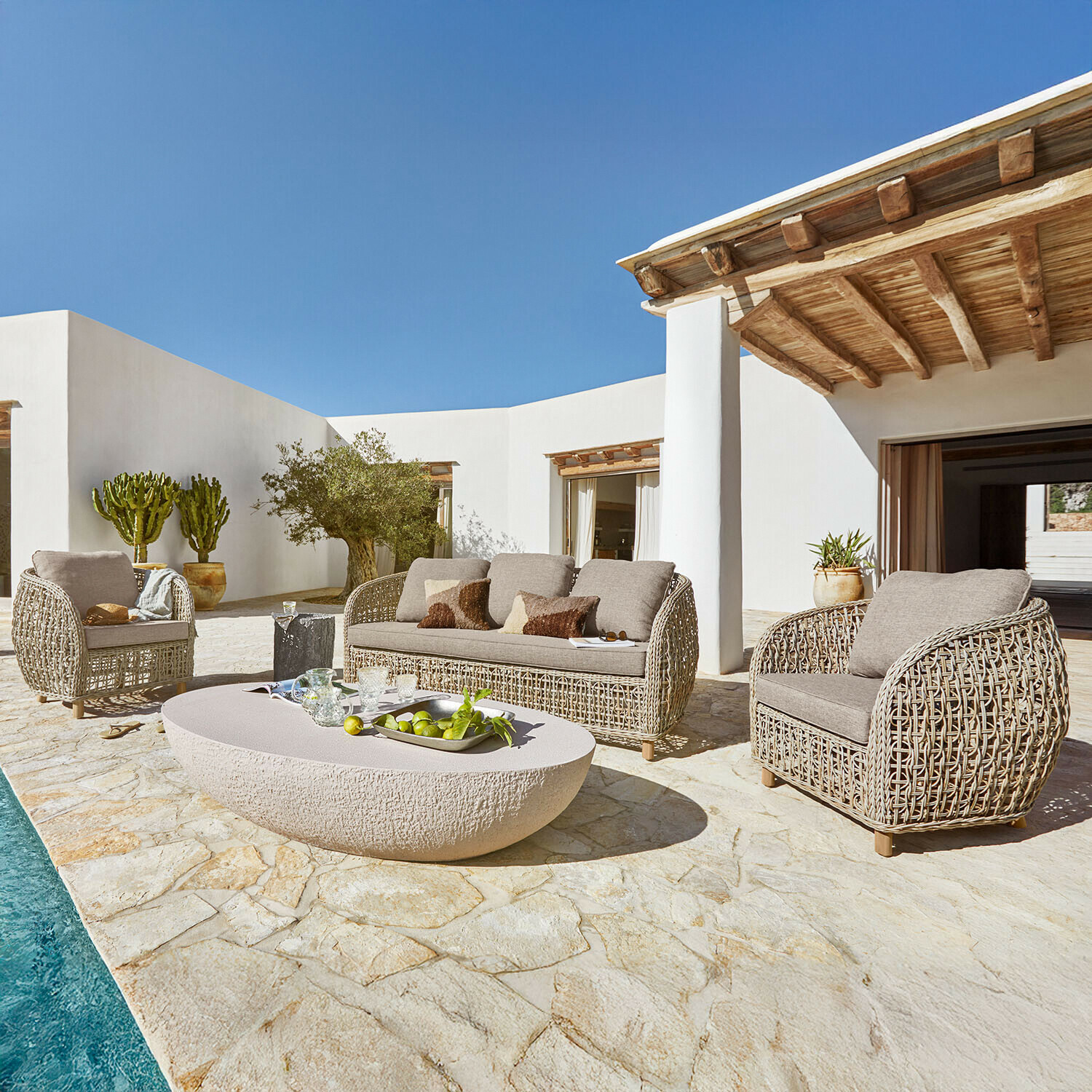 Grupo de asientos Ventiglio Conjunto de muebles de jardín de ratán beige con cojines en terraza de piedra junto a piscina soleada
