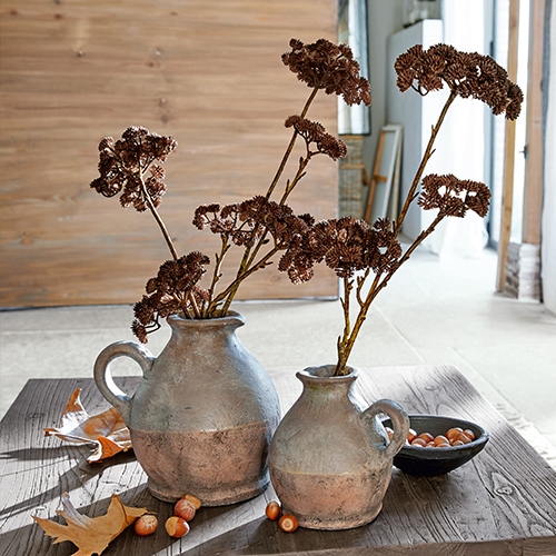 Dos jarras de cerámica gris marrón con flores secas sobre mesa de madera con avellanas
