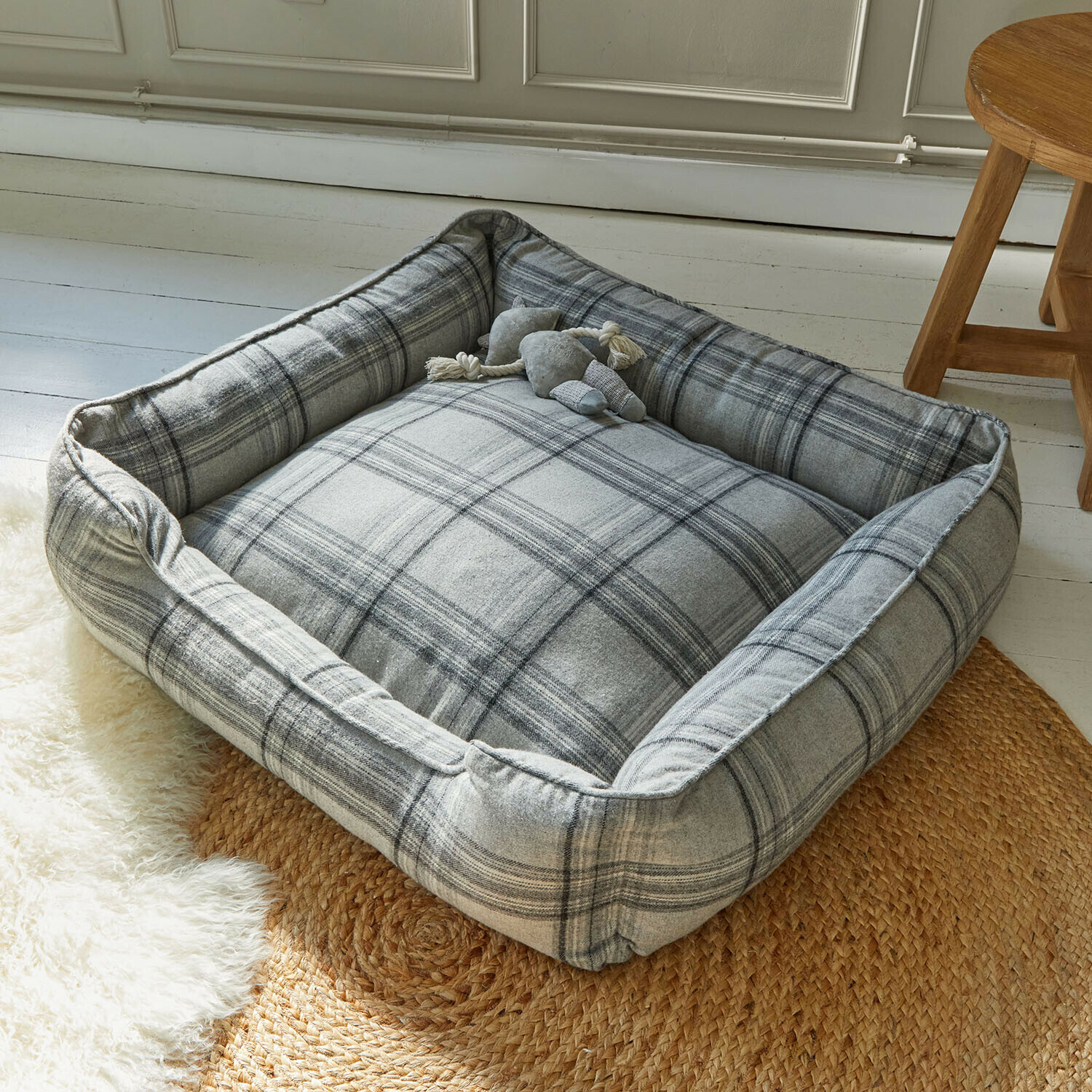 Cama para mascotas Creswyn Cama para perro gris a cuadros de tela suave sobre alfombra trenzada en habitación luminosa