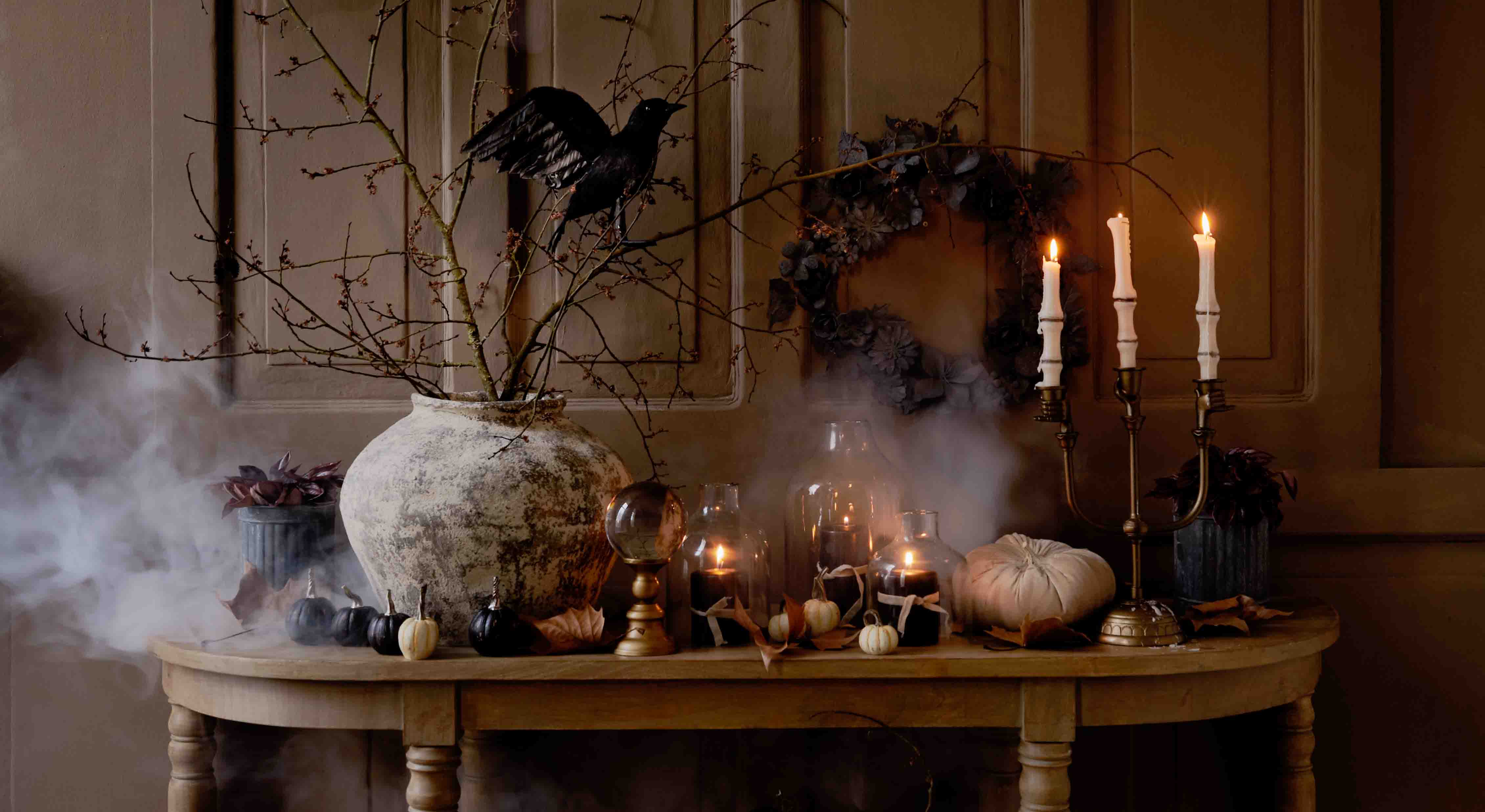Mesa rústica con decoración otoñal de calabazas, velas y ramas en jarrón de cerámica, iluminación ambiental