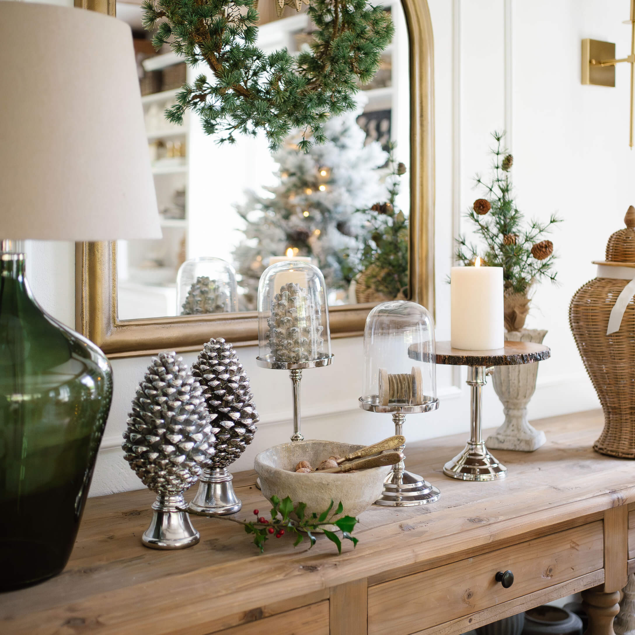 Decoraciones de piñas plateadas y vela sobre mesa de madera en interior rústico con acentos verdes