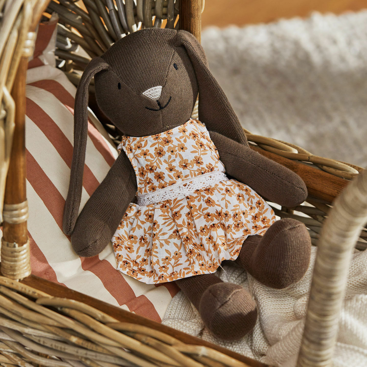 Peluche Pippaloo Conejo de peluche marrón con vestido floral en sillón de mimbre con cojín a rayas