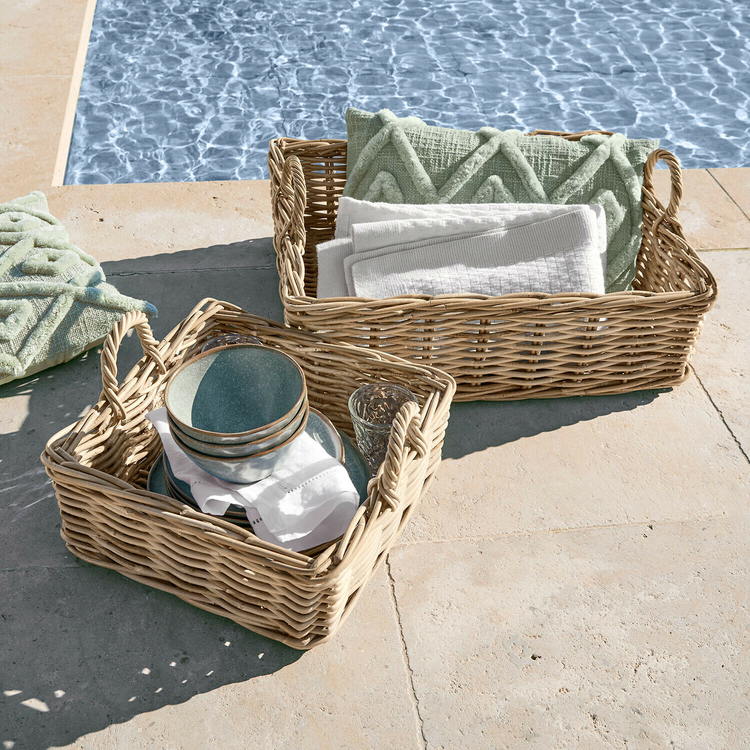 Set de 2 cestas Selwooden Dos cestas de mimbre con asas, con cojines verdes y toallas blancas junto a la piscina