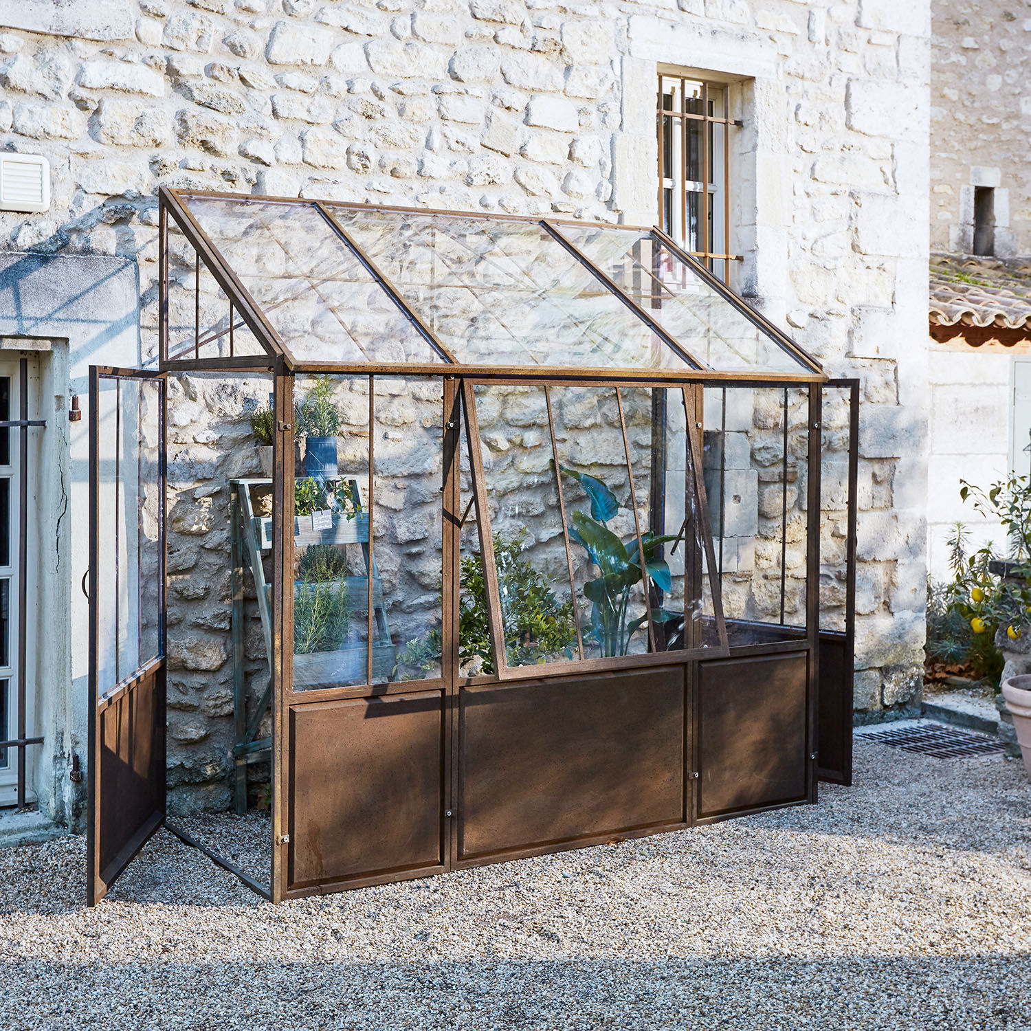 Invernadero de jardín con estructura metálica oxidada y paneles de vidrio para cultivo de plantas y hierbas