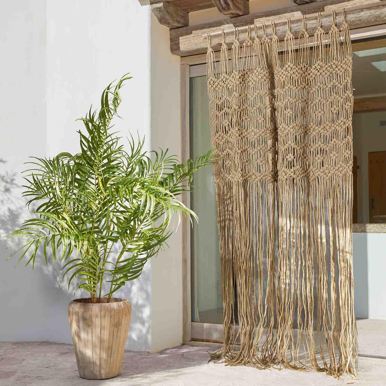 Cortina macramé beige de algodón con flecos largos en puerta terraza, planta en maceta al lado