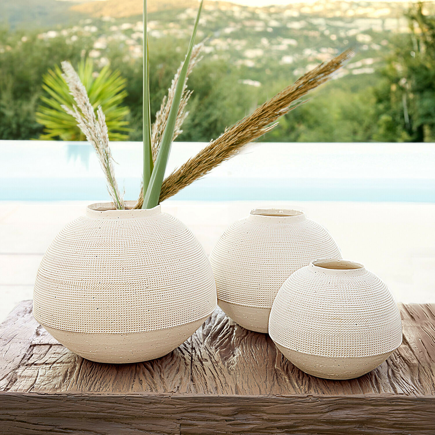 Set de 3 jarrones Émoliane Conjunto de tres jarrones redondos de cerámica beige sobre mesa de madera, decoración para interiores