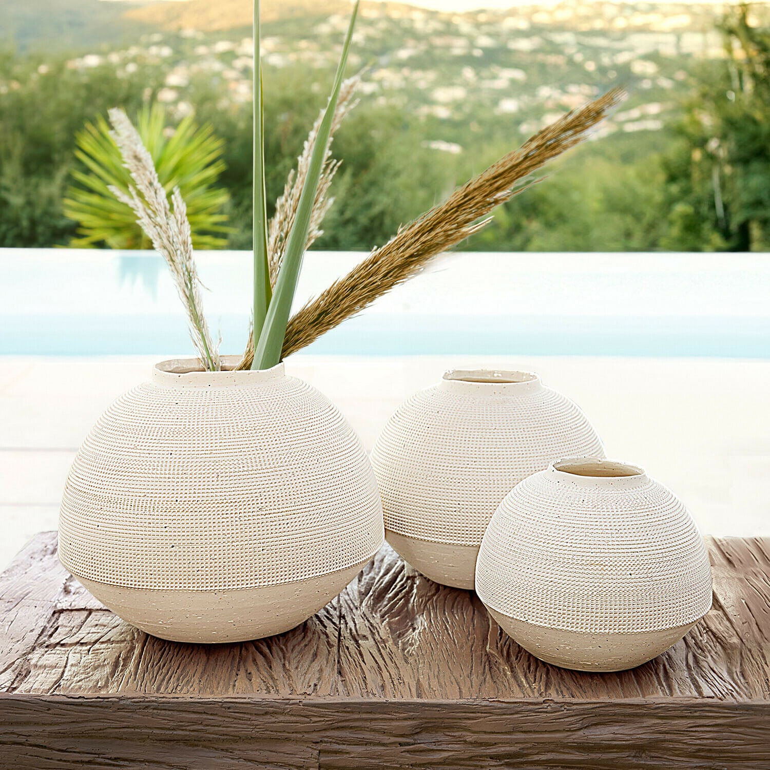 Set de 3 jarrones Émoliane Conjunto de tres jarrones redondos de cerámica beige sobre mesa de madera, decoración para interiores