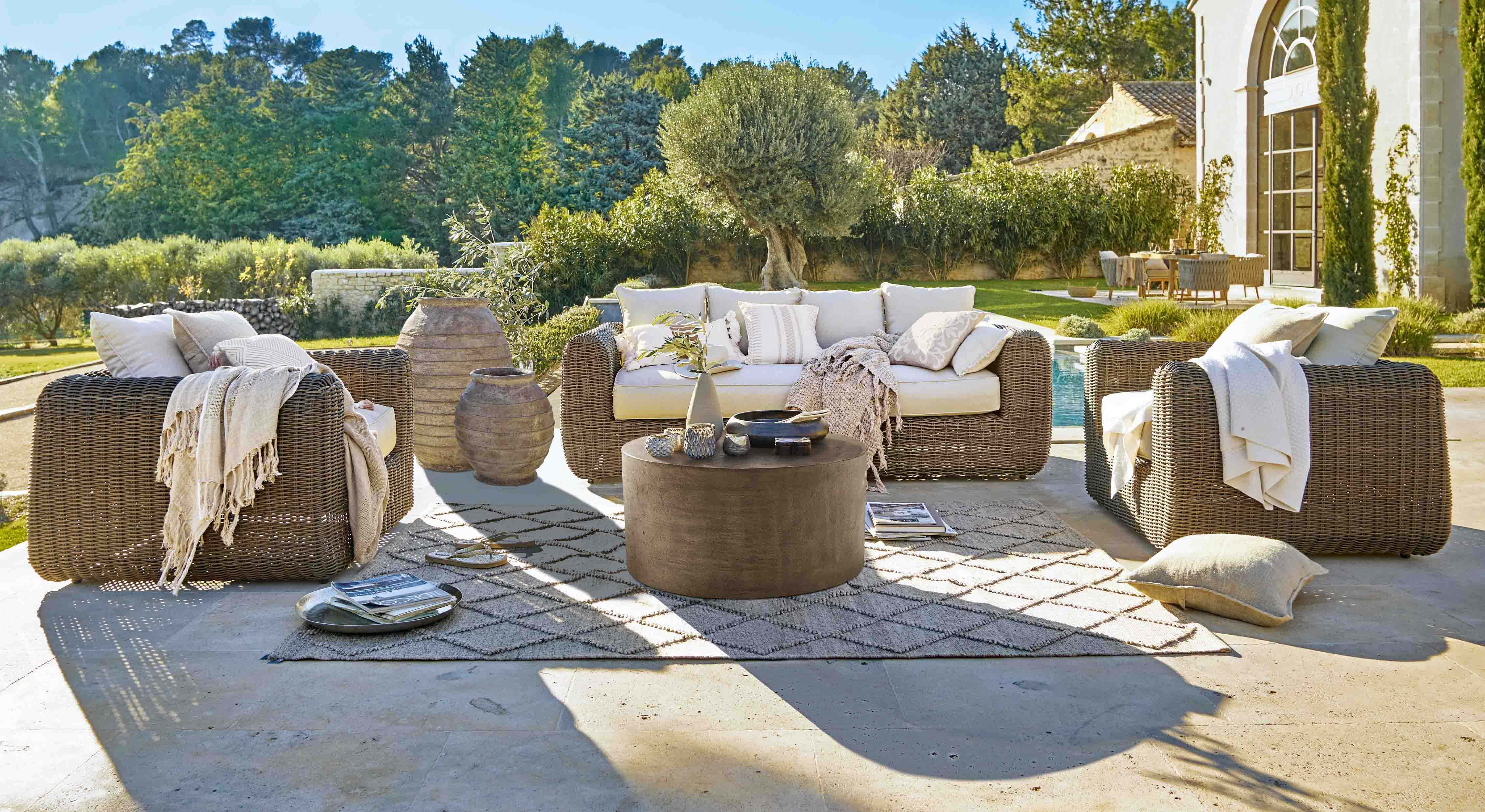 Conjunto de muebles de jardín de ratán marrón con cojines crema y mesa de centro redonda en terraza soleada