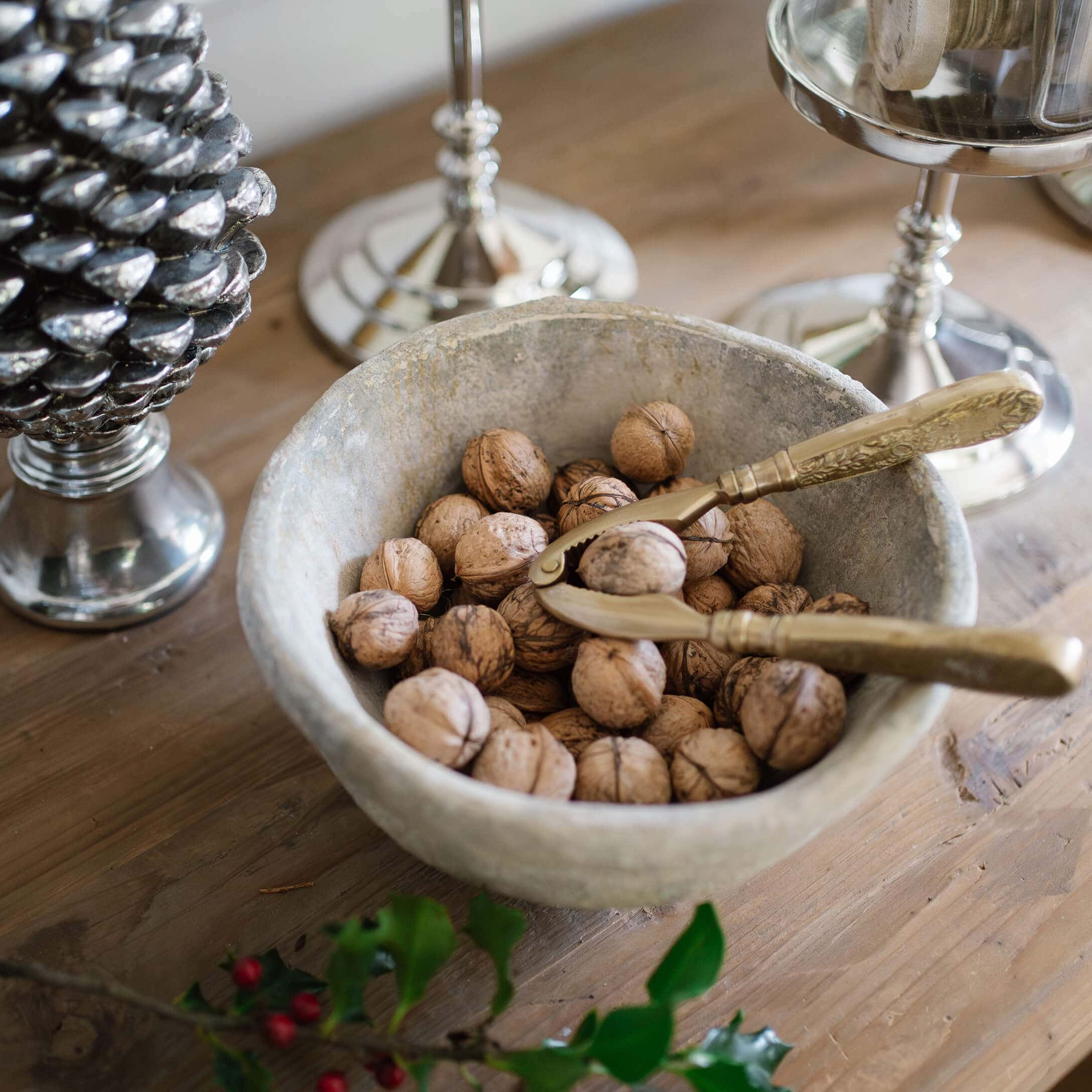 Cuenco de piedra con nueces y cascanueces dorado sobre mesa de madera rústica