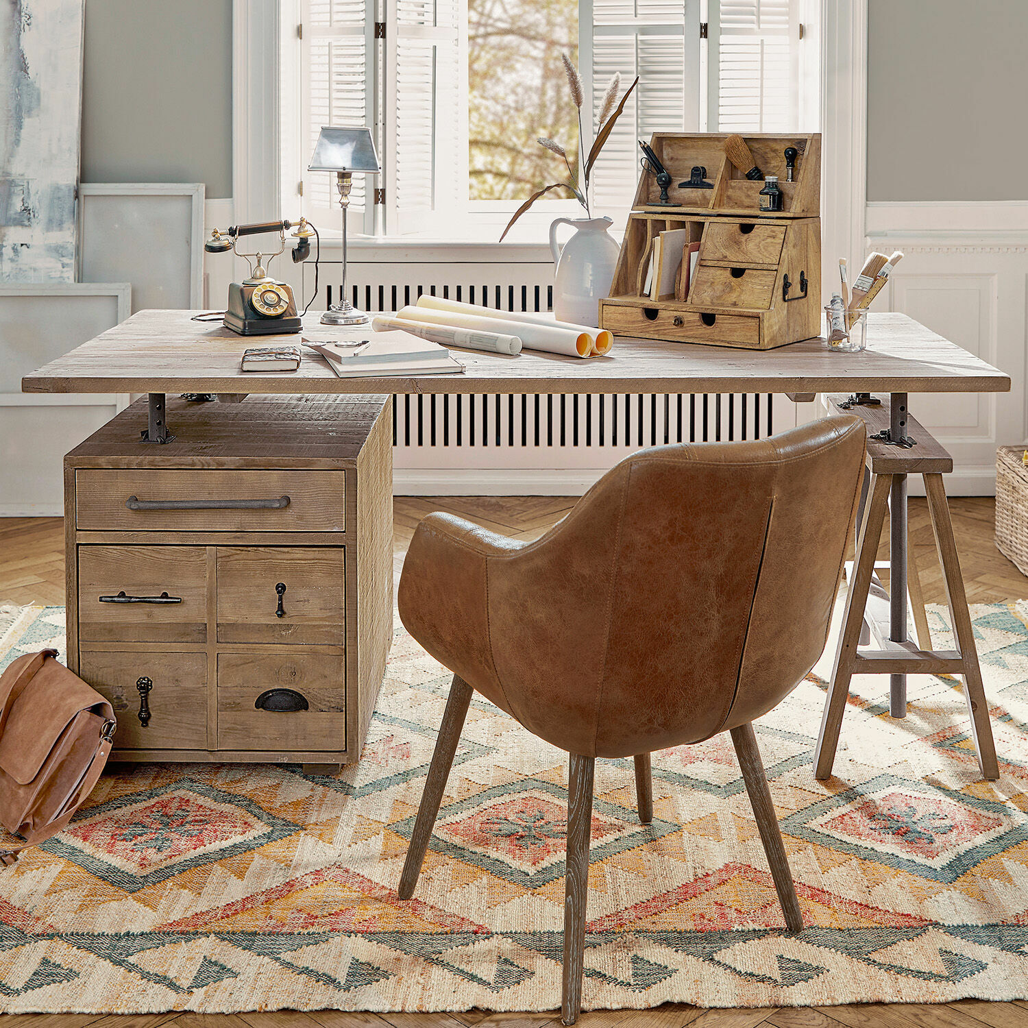 Escritorio Dawson Escritorio de madera con cajones y silla de cuero marrón sobre alfombra colorida en habitación luminosa