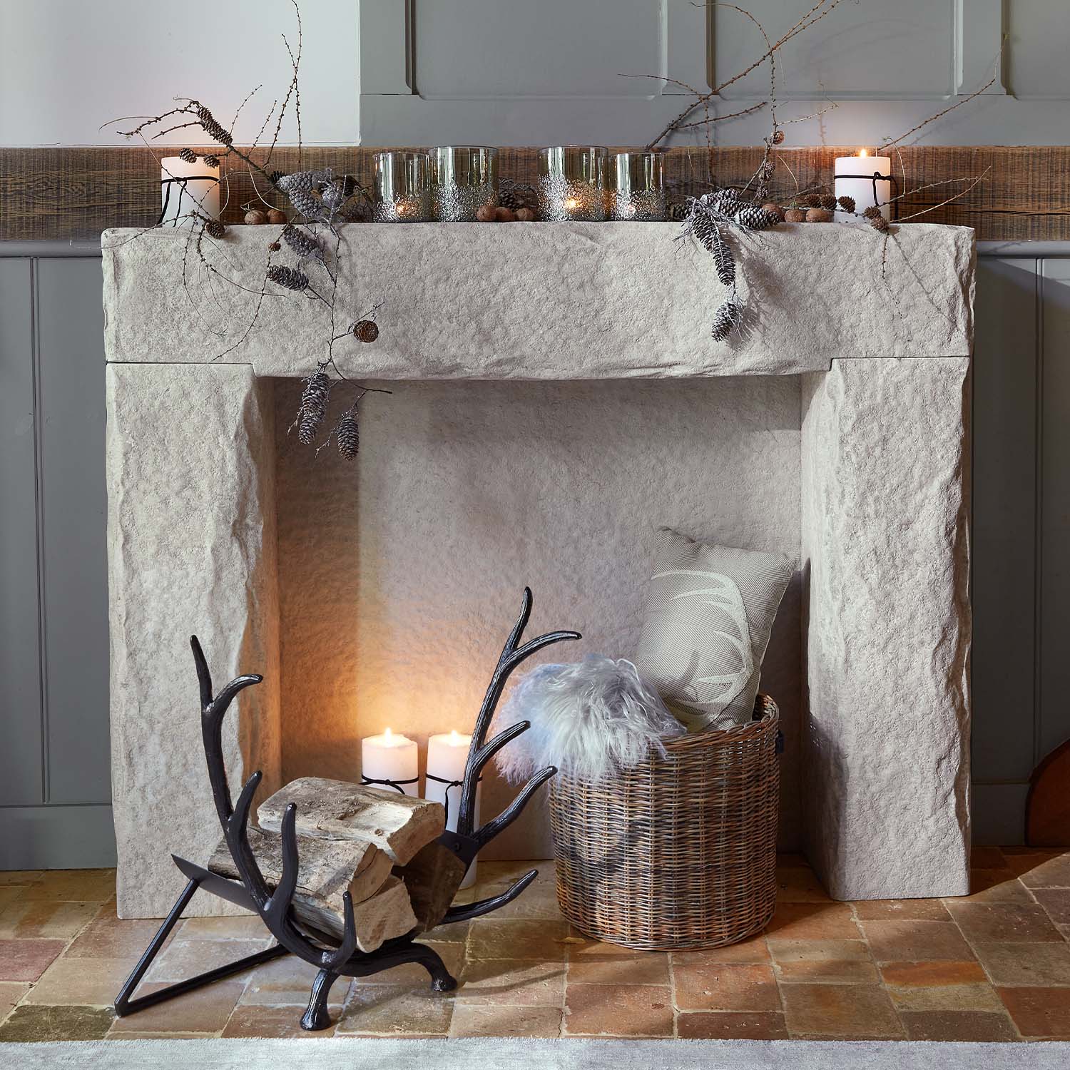 Chimenea de piedra con ramas decorativas, velas y cesta de mimbre con cojín y manta de piel sintética
