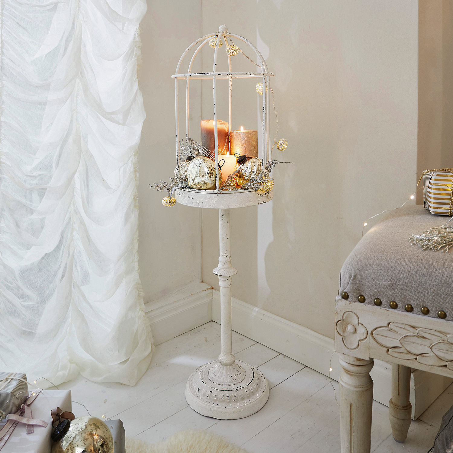 Soporte metálico blanco con jaula y velas decoradas con adornos dorados para interiores festivos