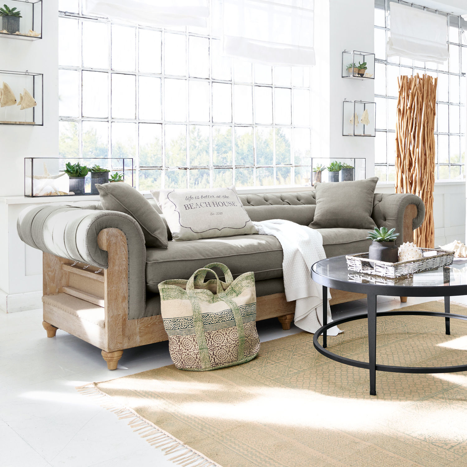 Sofá Kanani Sofá gris con estructura de madera en sala luminosa con decoración y mesa de centro redonda