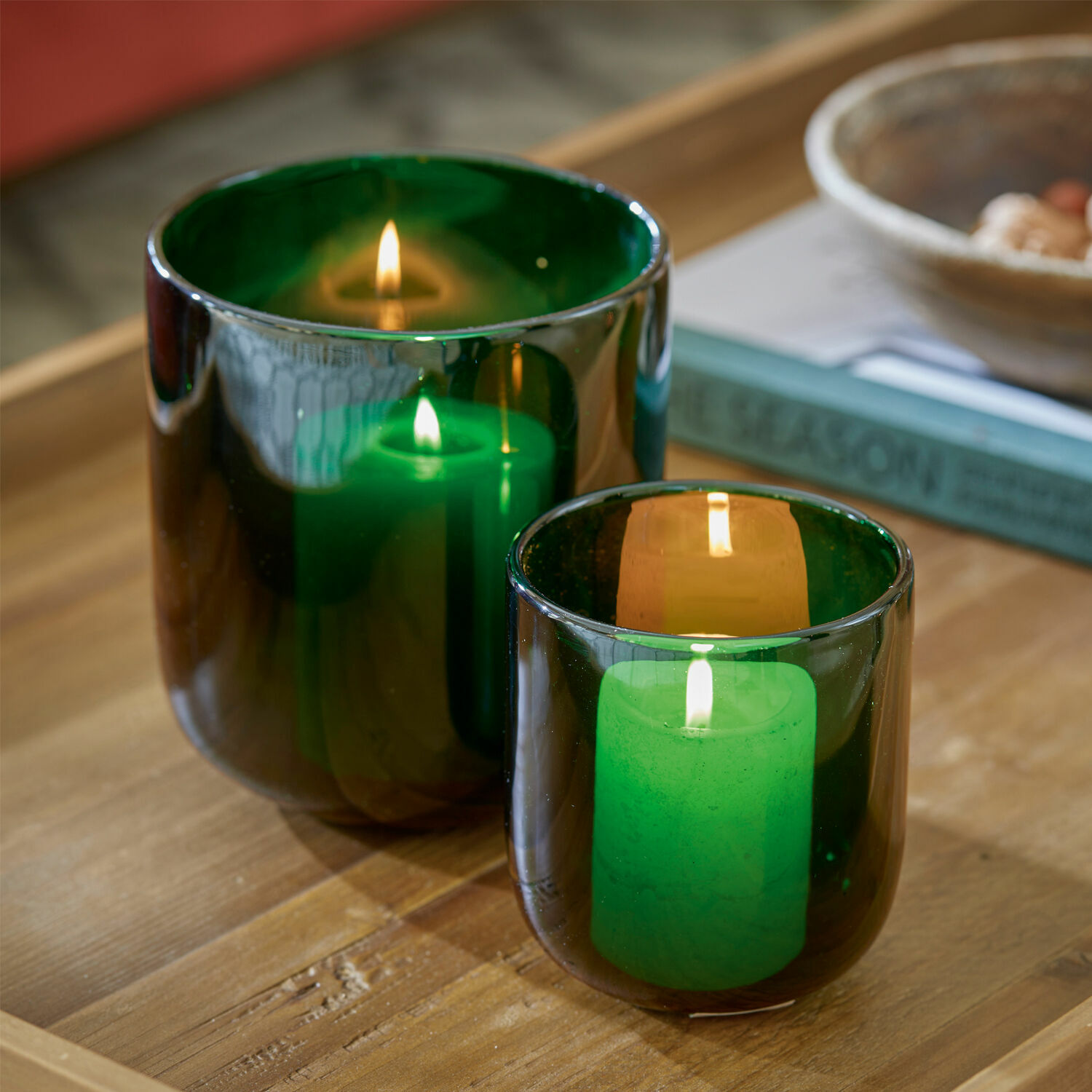 Set de 2 farolillos Theodor Dos portavelas de vidrio verde con velas encendidas sobre mesa de madera, decoración interior