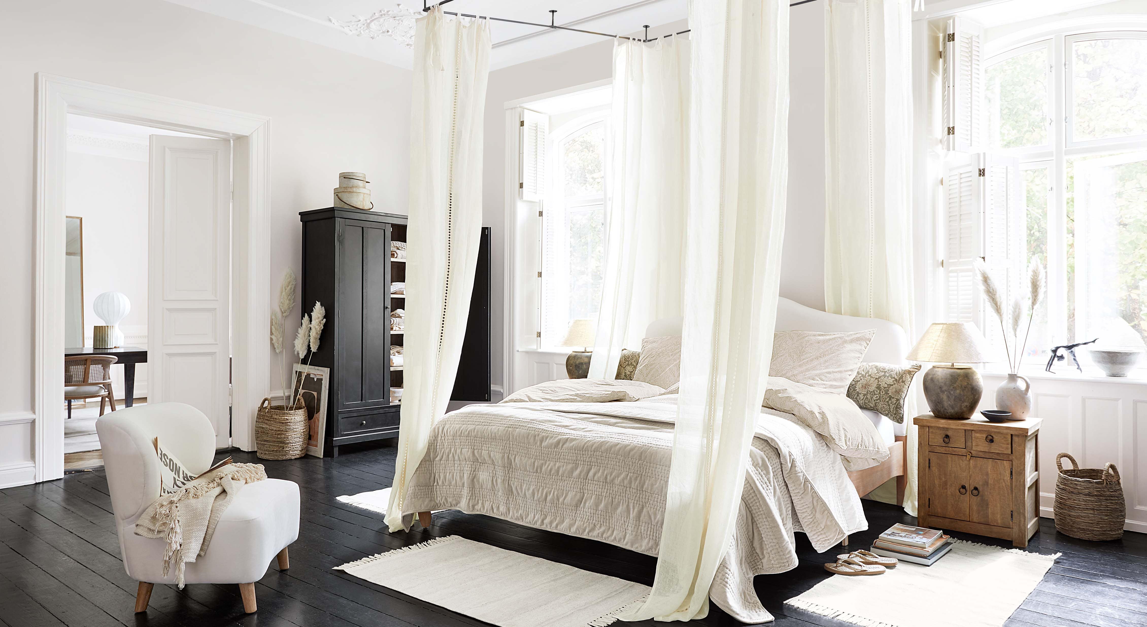 Dormitorio acogedor con cama con dosel, ropa de cama beige claro y muebles de madera estilo escandinavo