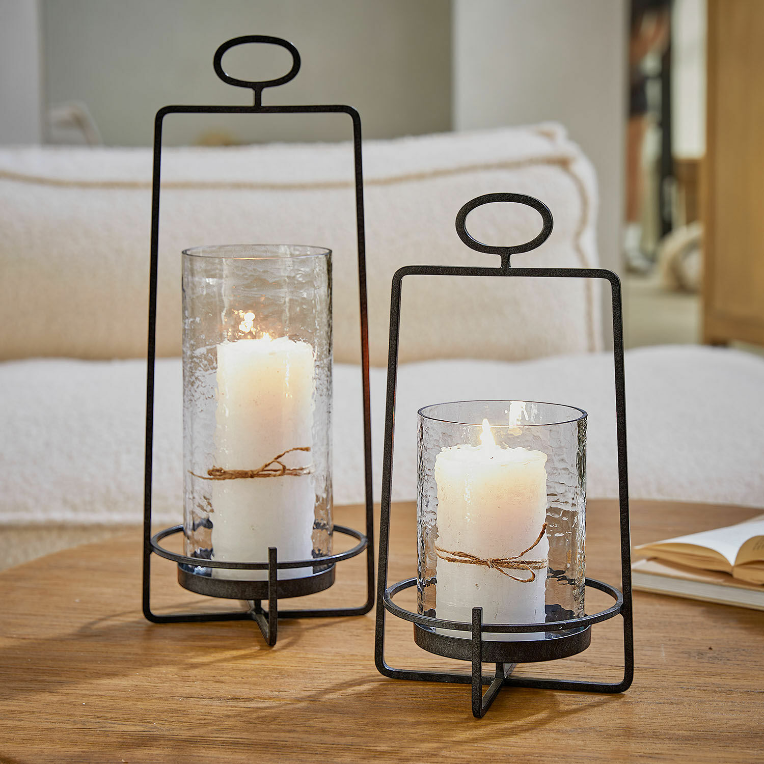 Set de 2 farolillos Zevara Dos faroles de metal con vidrio transparente y velas blancas sobre mesa de madera en sala de estar