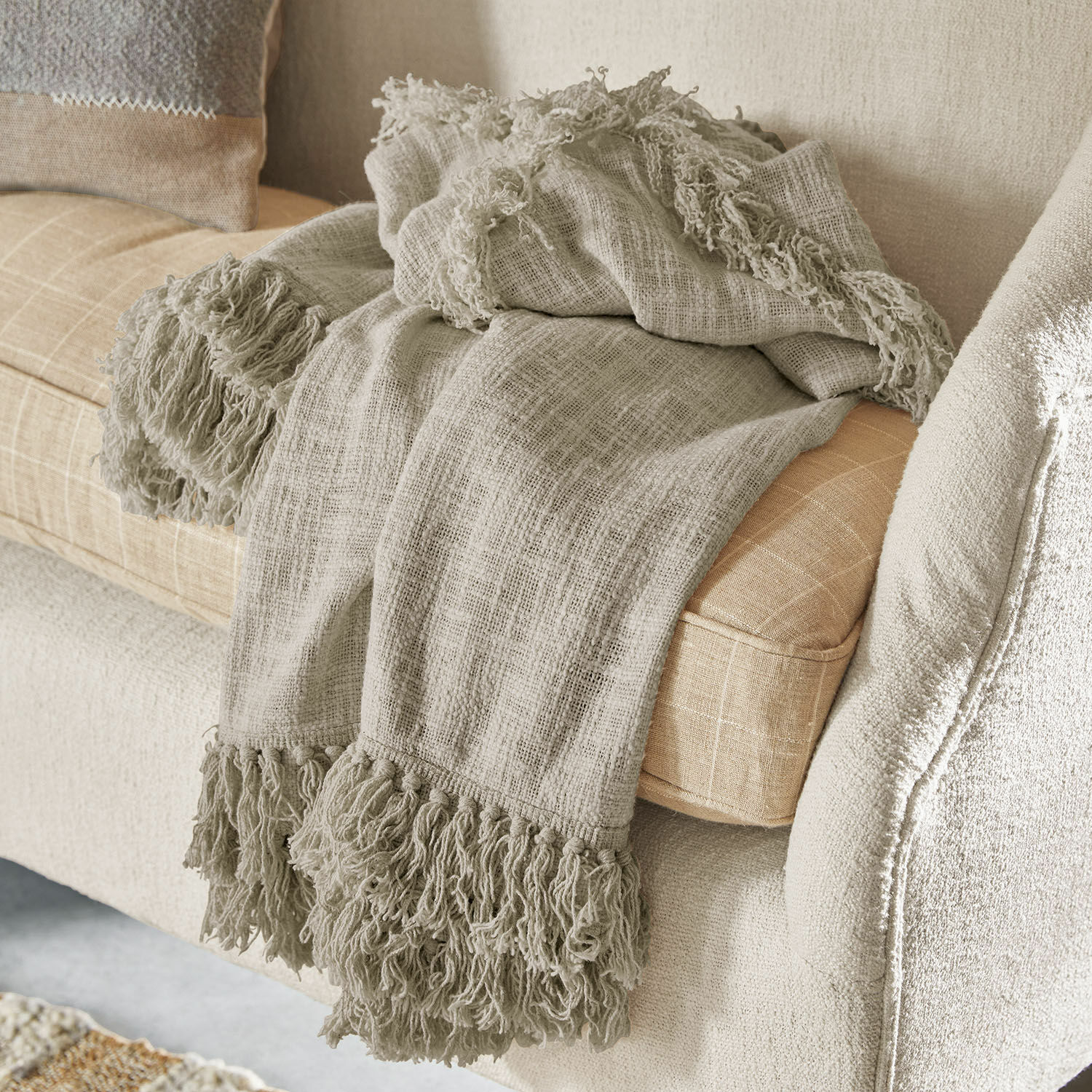 Plaid Freya Manta beige con flecos de material suave sobre sofá claro, decoración acogedora