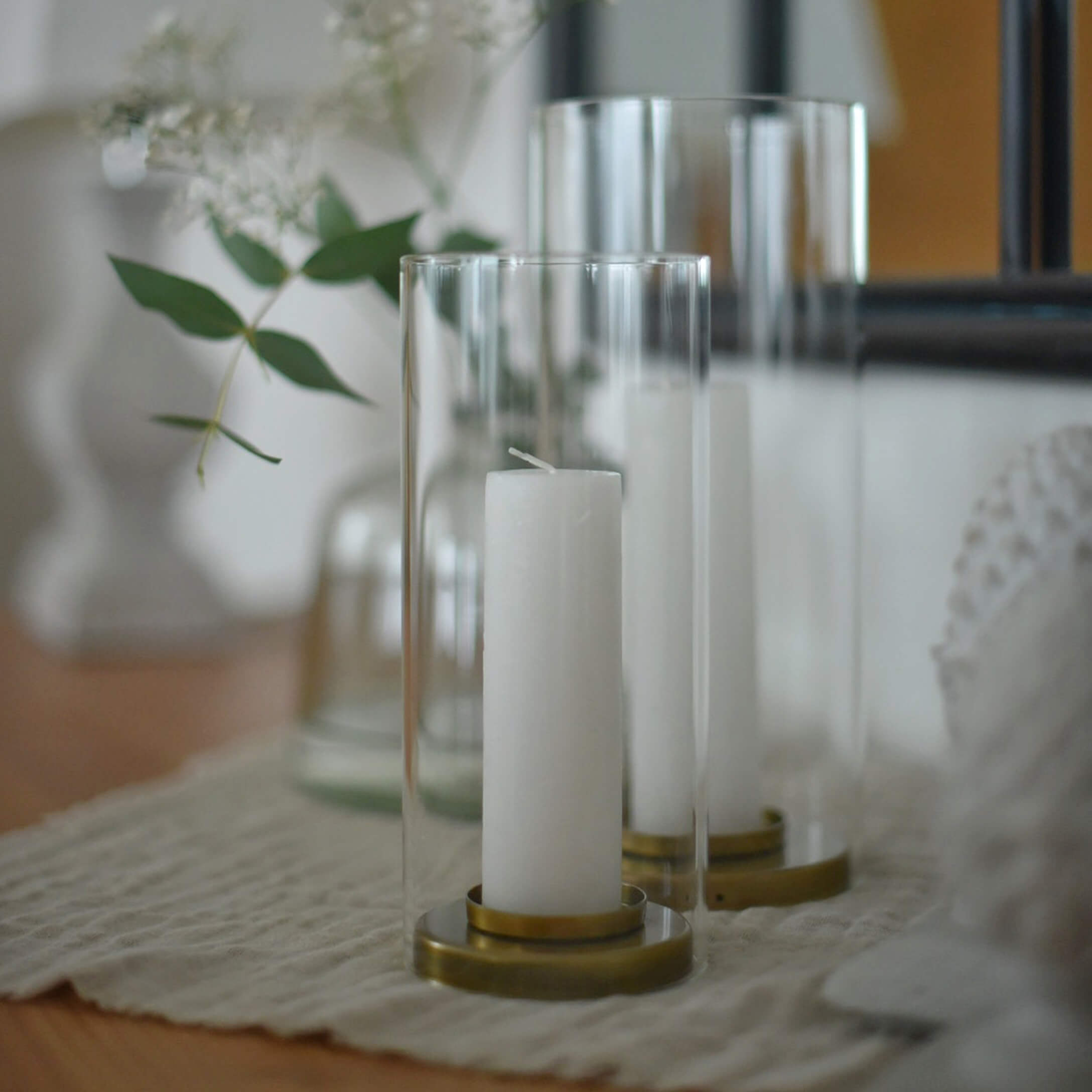 Velas blancas en faroles de vidrio transparente con base de latón sobre mantel beige