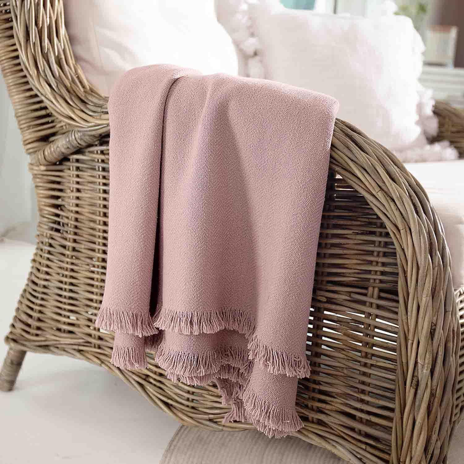 Manta rosa de material suave con flecos sobre sillón de mimbre, decoración y confort en hogar