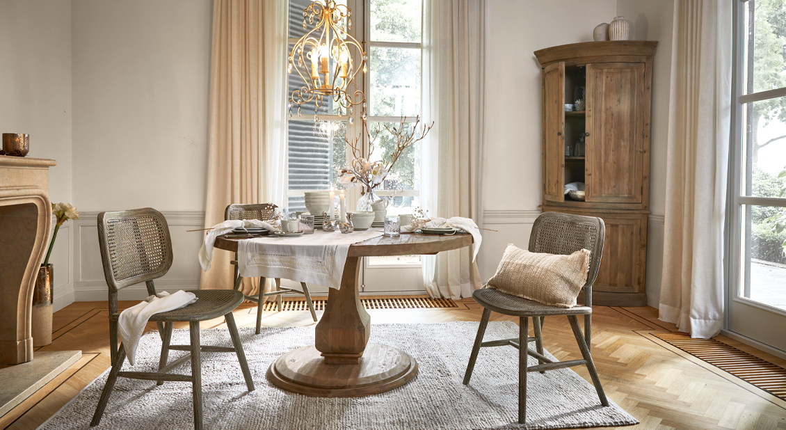 Comedor con mesa redonda de madera y sillas de mimbre en tonos naturales, cortinas claras