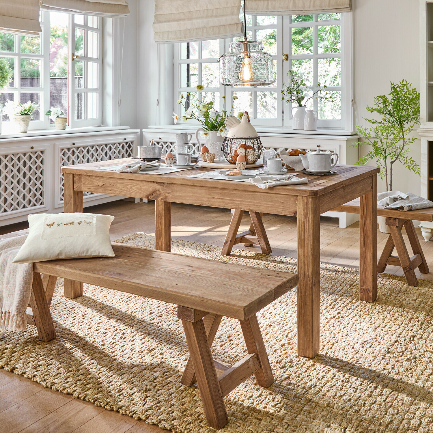 Mesa Amherst Comedor con mesa y bancos de madera sobre alfombra natural, interior luminoso con decoraciones y luz