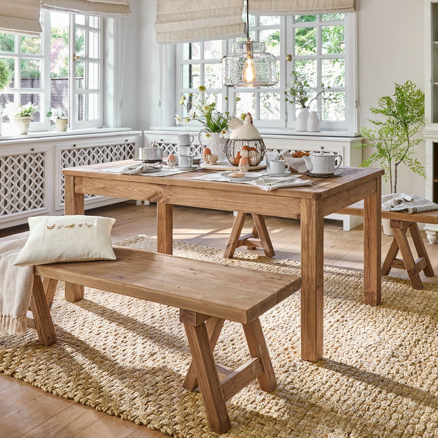 Mesa Amherst Comedor con mesa y bancos de madera sobre alfombra natural, interior luminoso con decoraciones y luz