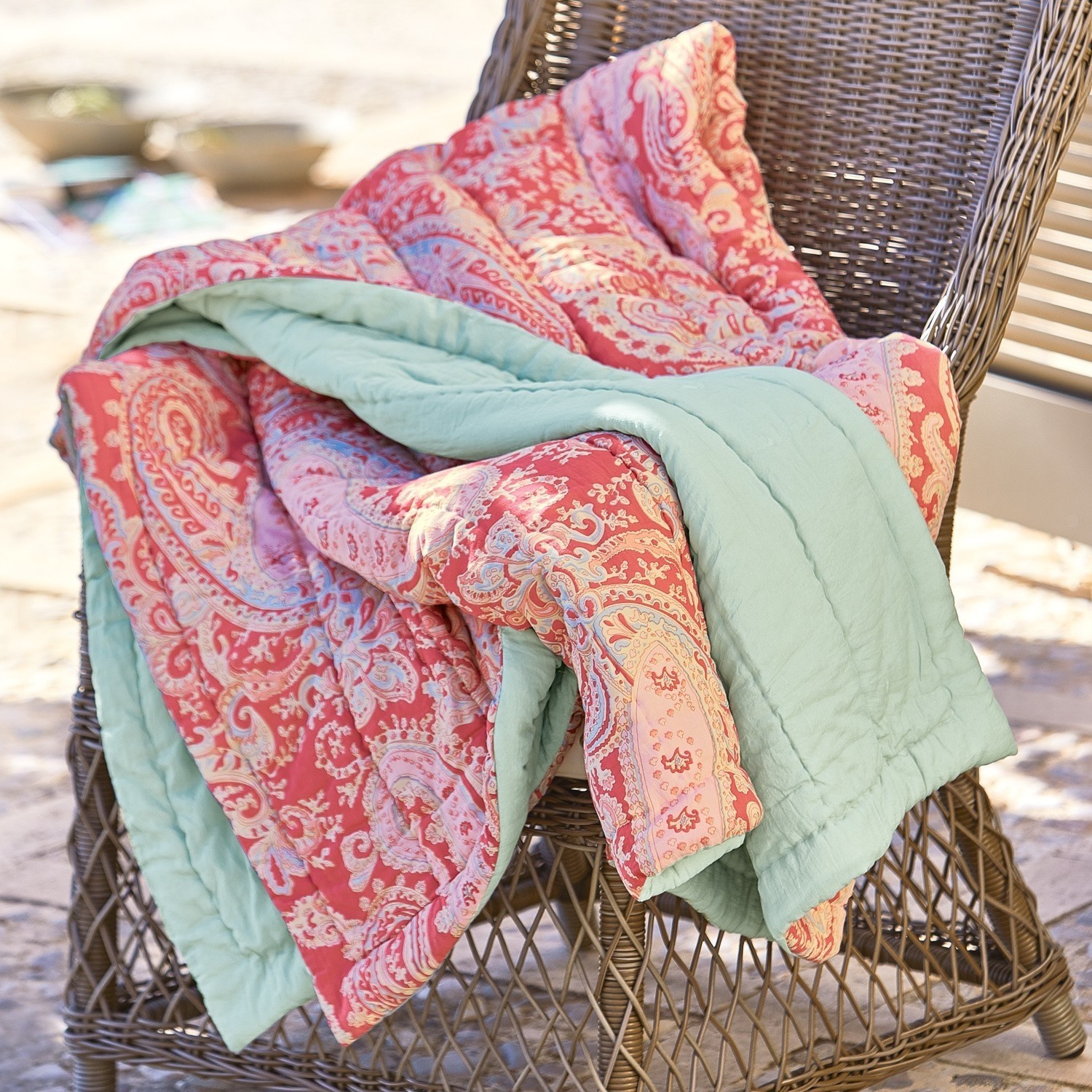 Plaid Aram Manta reversible con diseño paisley rojo y rosa con forro verde suave sobre silla de mimbre