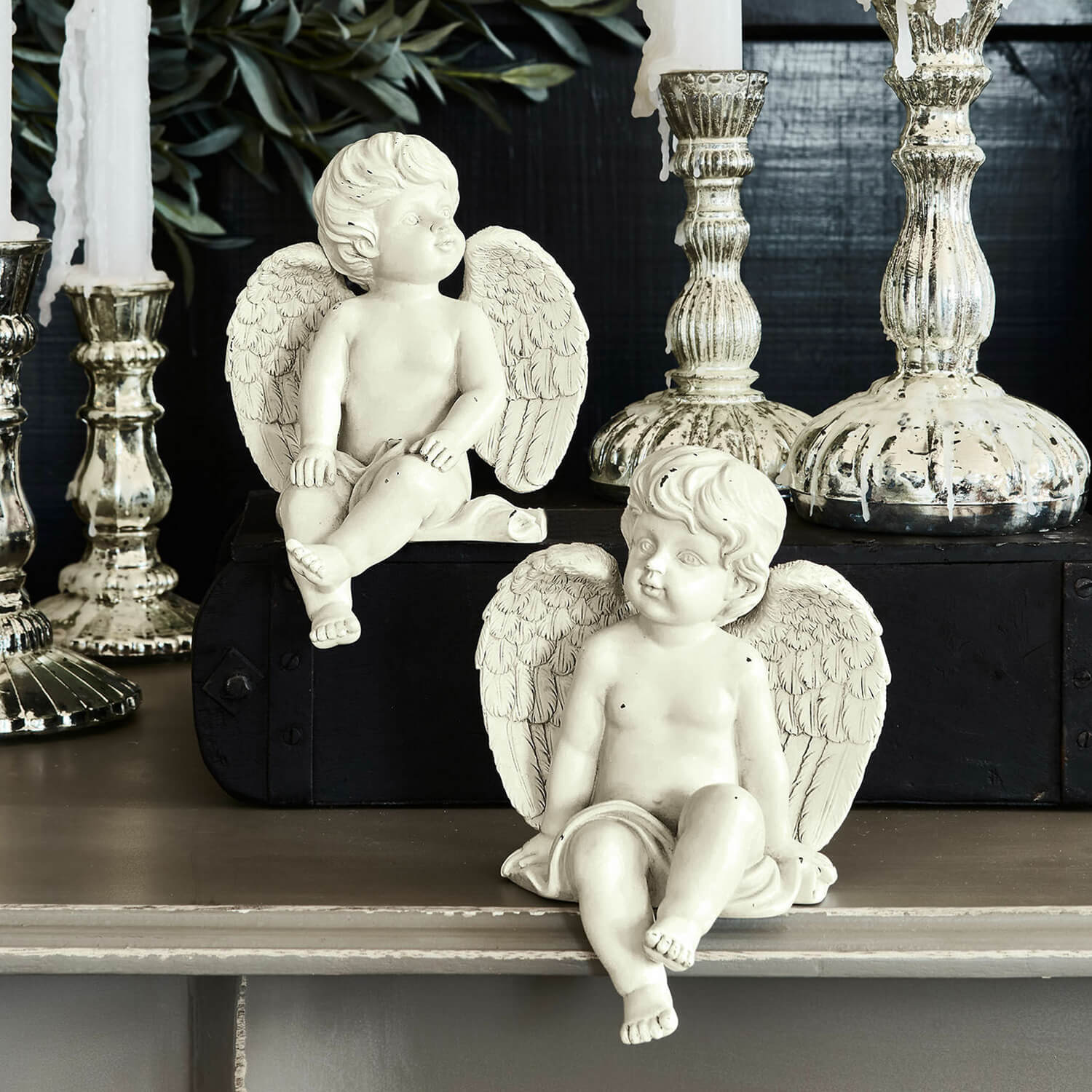 Dos figuras blancas de ángeles de resina frente a candelabros plateados, decoración de interiores