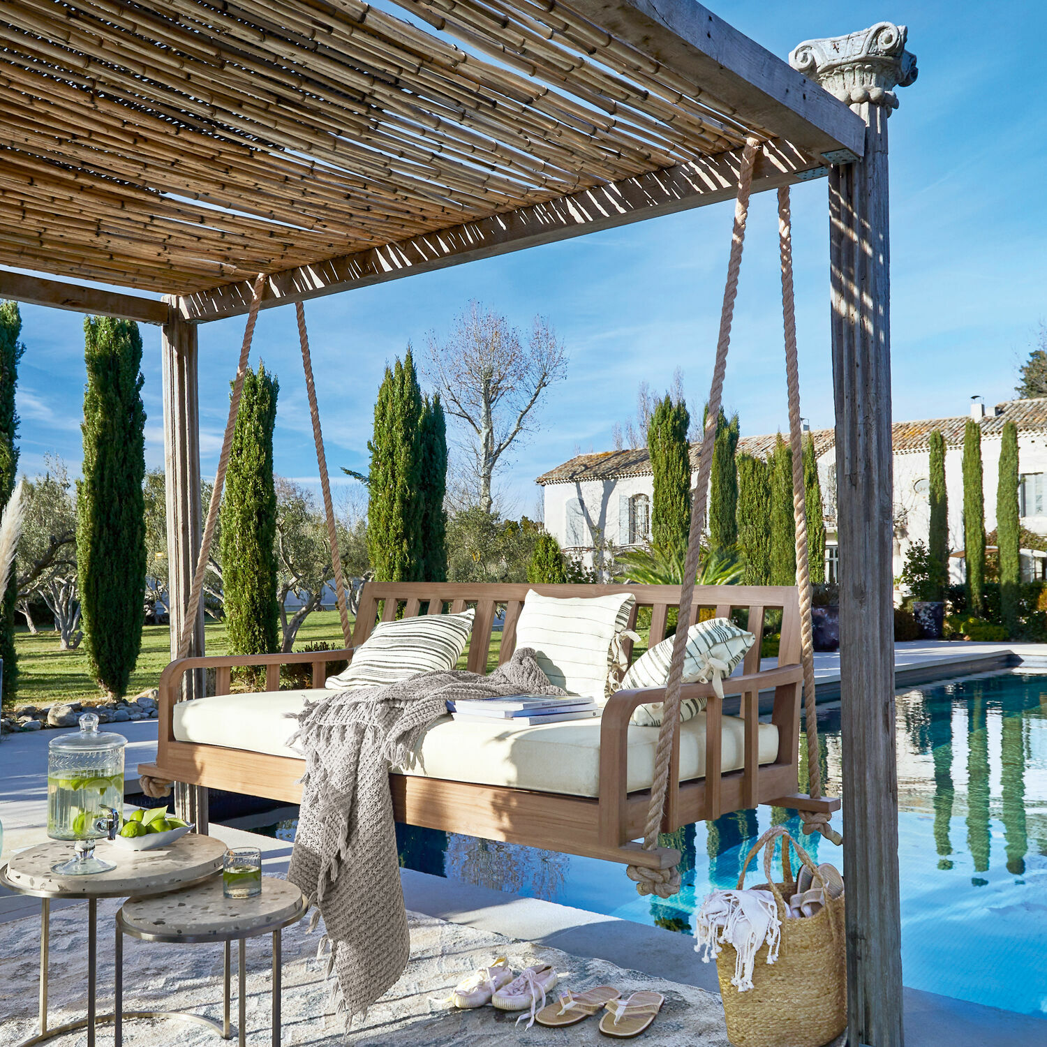 Banco colgante Travert Columpio de jardín de madera de teca con cojín crema y cojines a rayas junto a la piscina