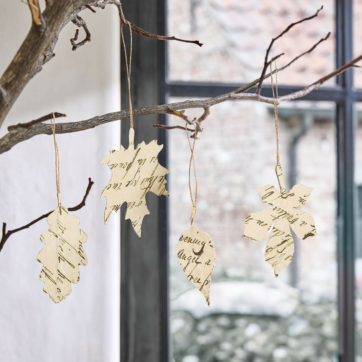 Set de 4 colgantes Fleuriene Adornos colgantes de hojas de papel con escritura, colgados de una rama frente a una ventana
