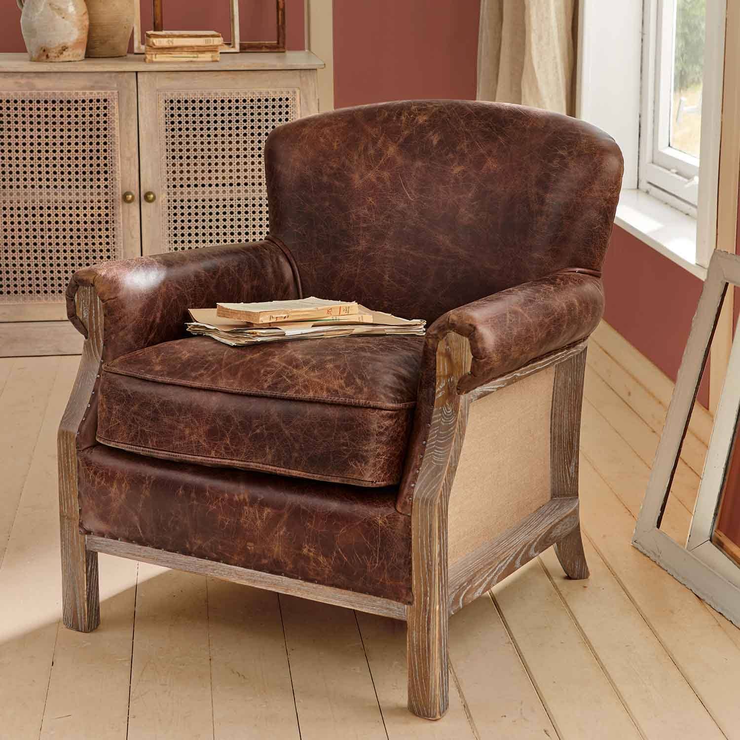 Sillón marrón de cuero envejecido con estructura de madera en interior rústico con libros