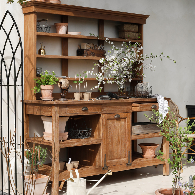 Mueble de jardín de madera con estantes, macetas y ramas floridas, decorado con herramientas de jardinería