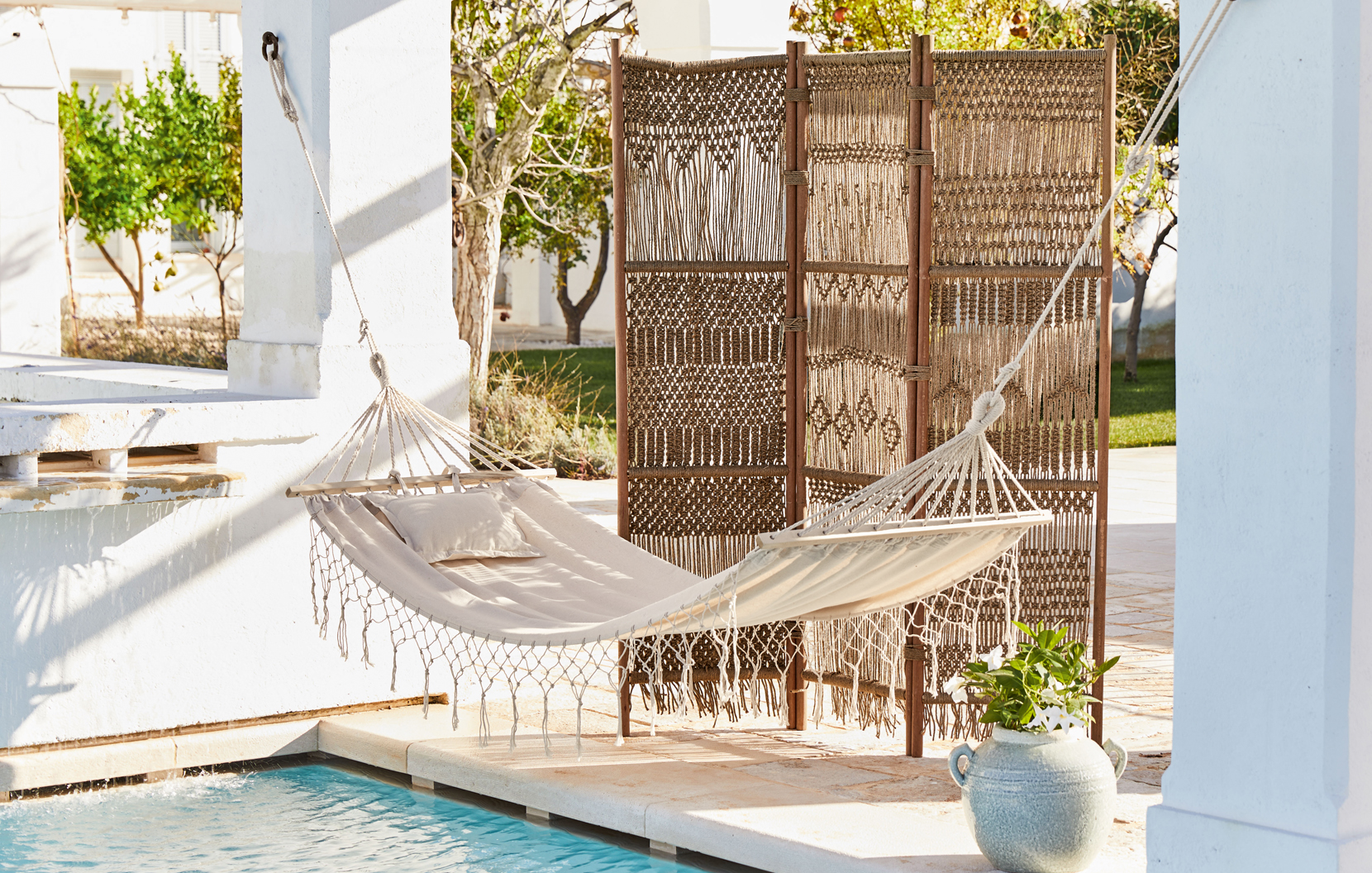 Hamaca beige con cojín y biombo tejido en terraza junto a piscina estilo bohemio