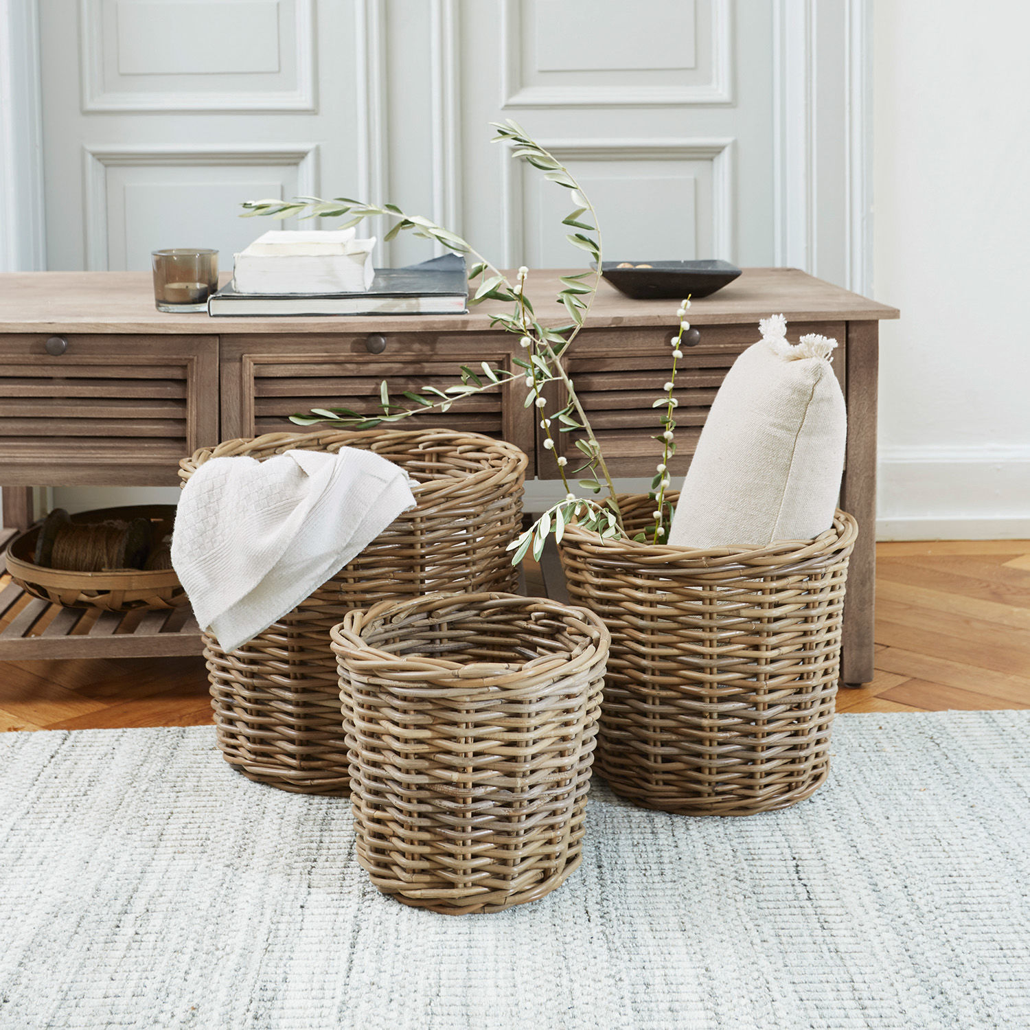 Set de 3 cestas Avar Conjunto de tres cestas de mimbre en color natural para almacenamiento en casa sobre alfombra clara.