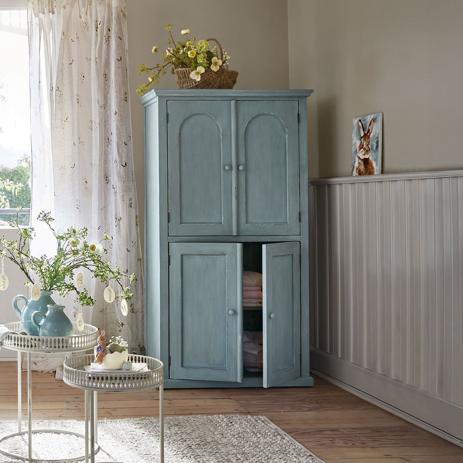 Armario de madera azul con dos pares de puertas en una habitación luminosa y acogedora con decoración primaveral