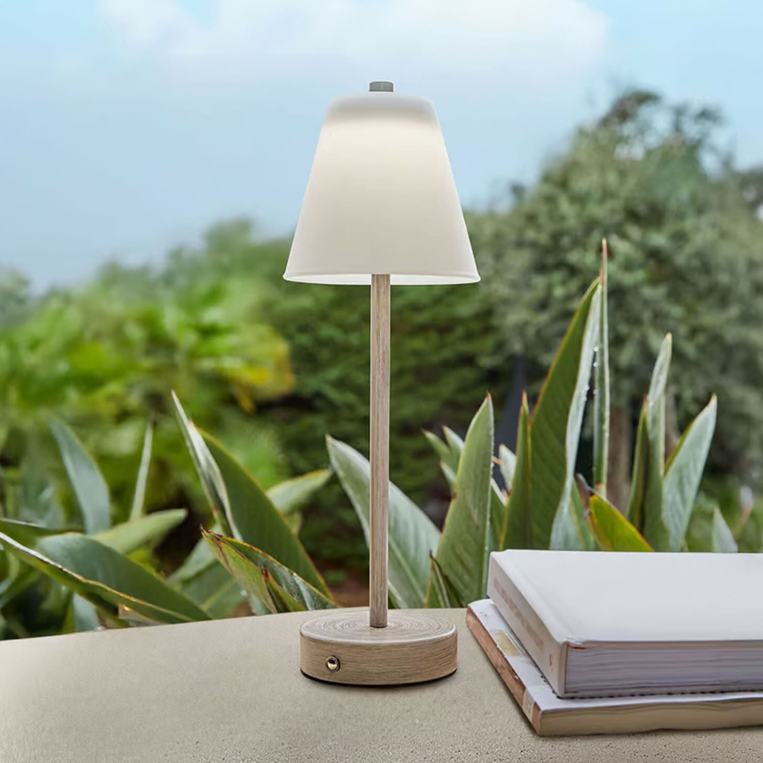 Lámpara de mesa de madera clara con pantalla blanca frente a plantas verdes, decoración interior