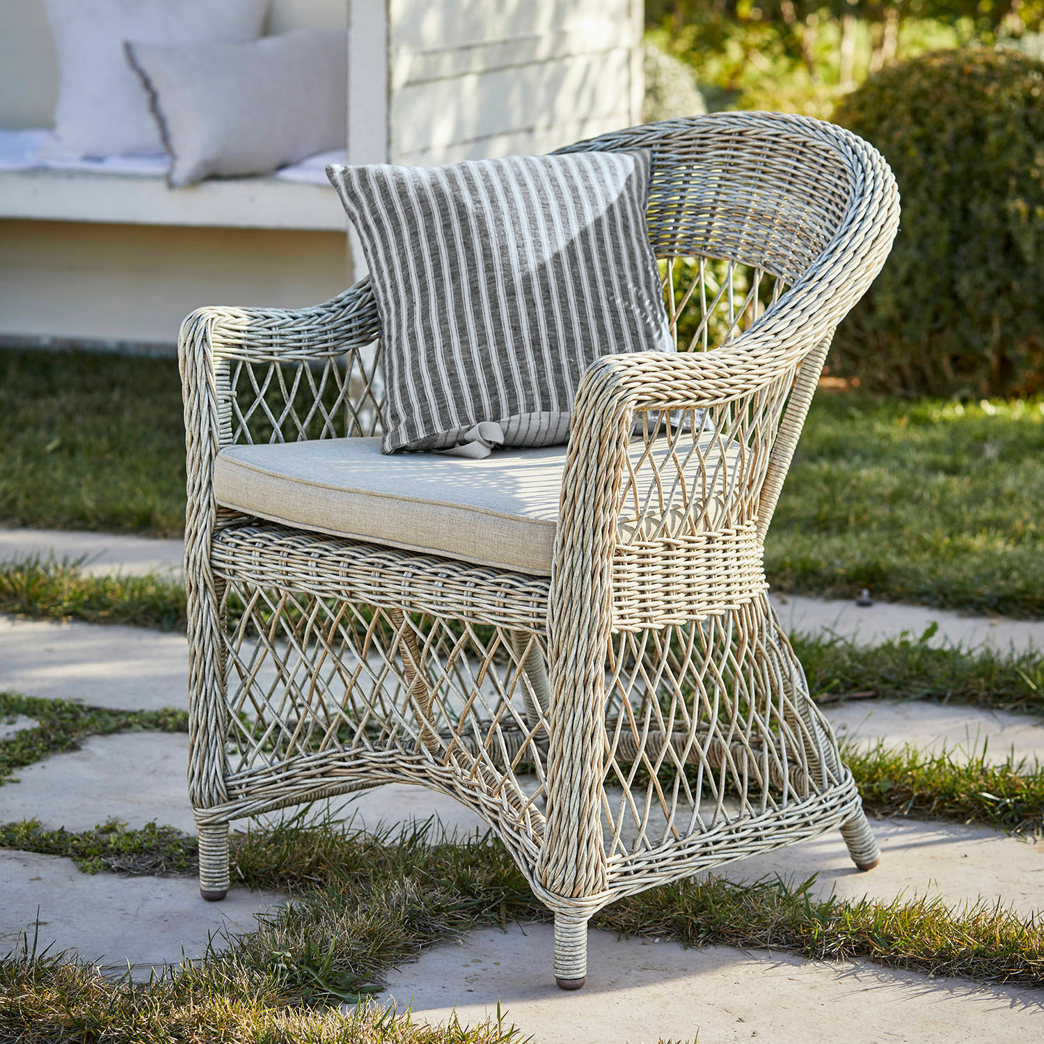 Sillón de jardín de ratán claro con cojín a rayas, perfecto para relajarse al aire libre