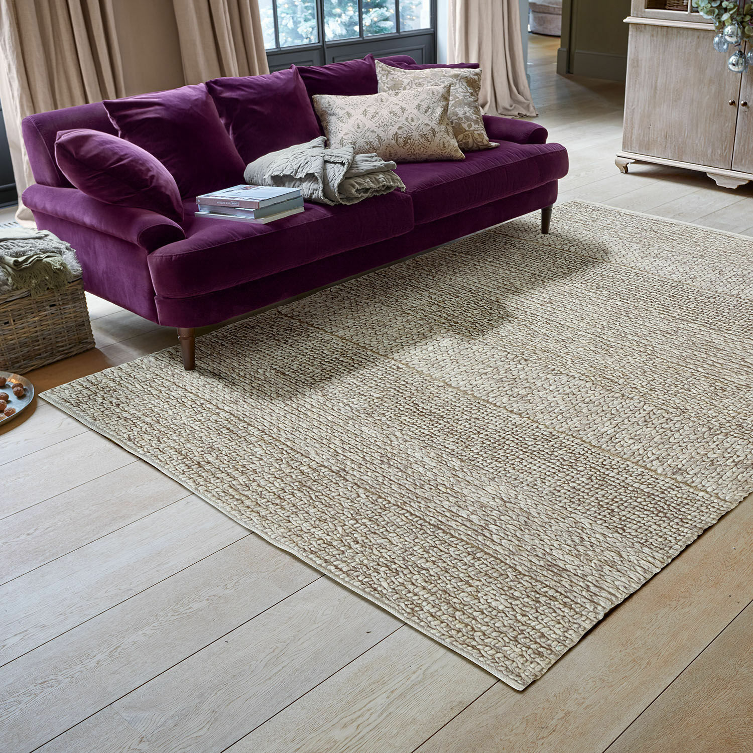 Alfombra Welezas Alfombra beige de material natural con textura trenzada en sala moderna con sofá morado
