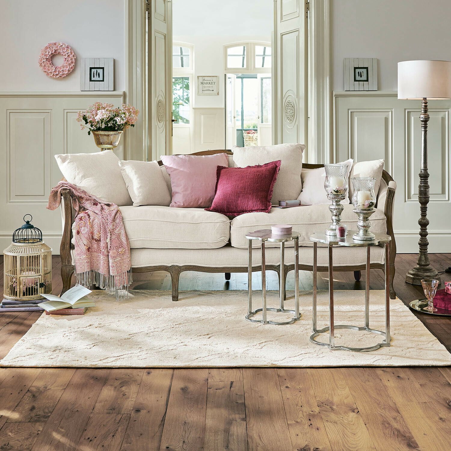 Sofa Monneville Sofá beige con marco de madera y cojines rosas en salón elegante con alfombra y mesas auxiliares