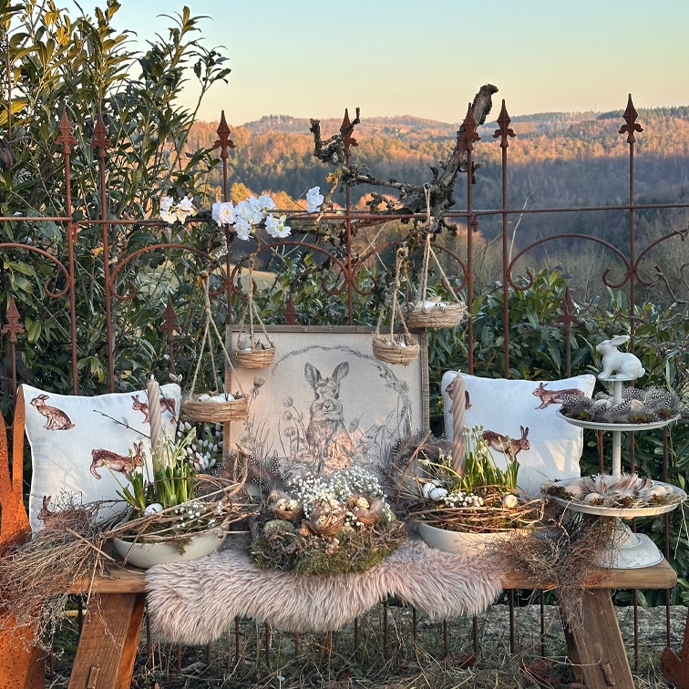 Decoración rústica de Pascua con cojines de conejo, cestas de mimbre y flores naturales sobre un banco de madera