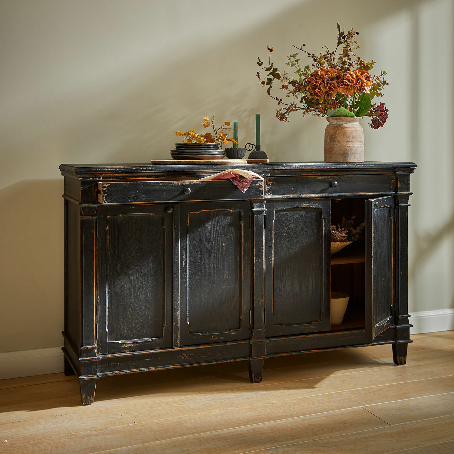 Aparador Chaveline Aparador de madera negra envejecida con puertas decorativas sobre suelo de madera clara.