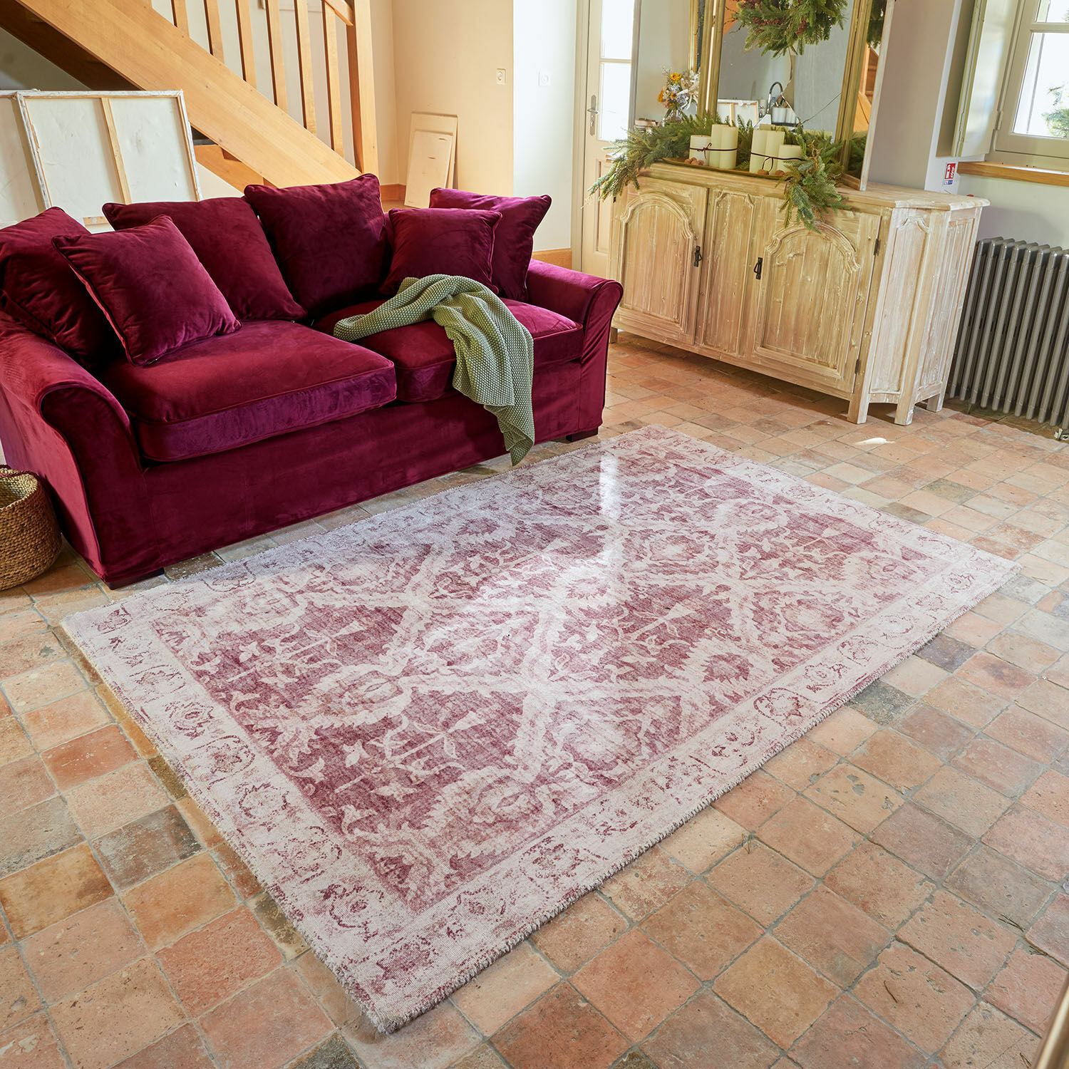 Alfombra Mirellis Alfombra decorativa en tonos rosa y blanco frente a un sofá de terciopelo burdeos en sala de estar