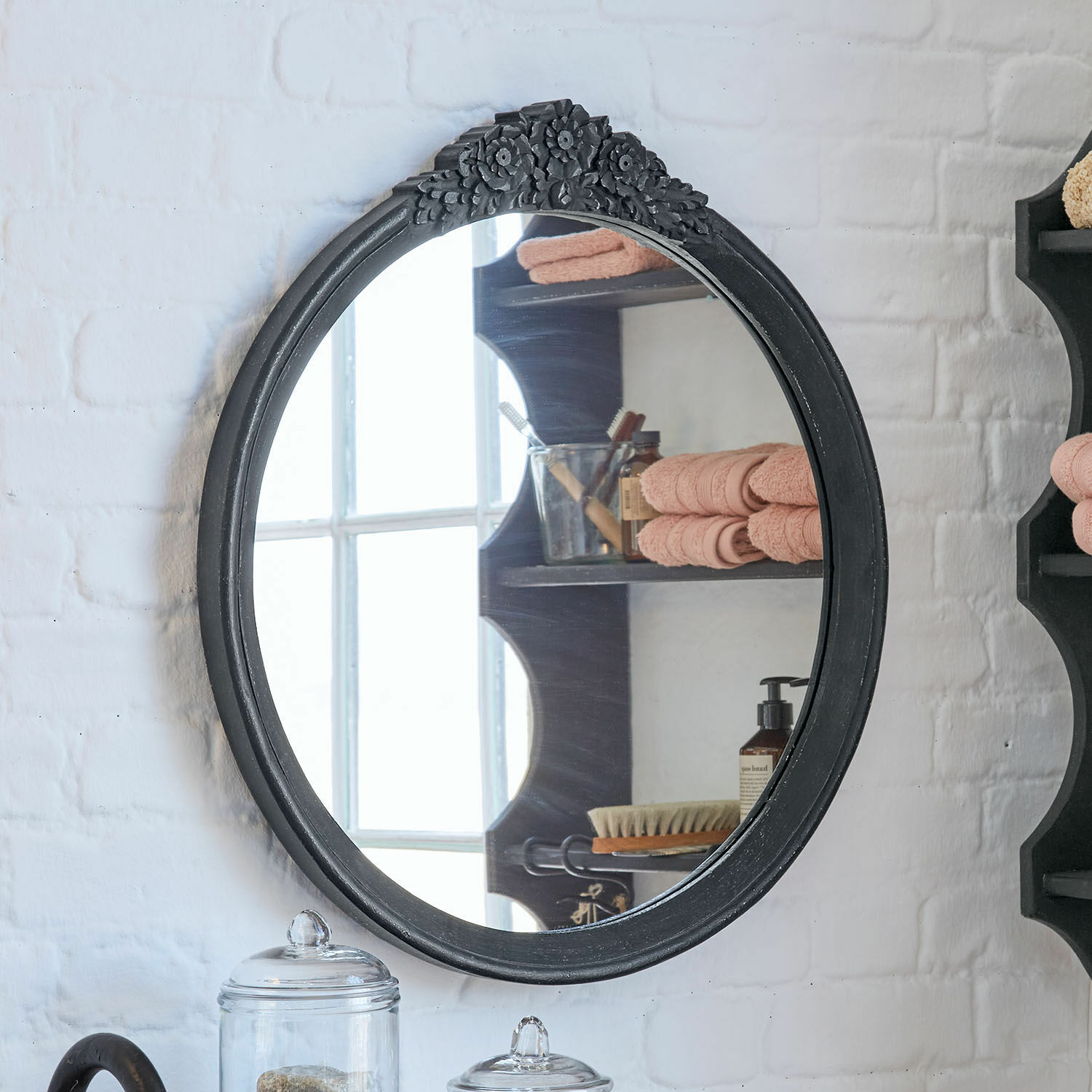 Espejo ovalado con marco de madera negra y adorno floral superior para baño