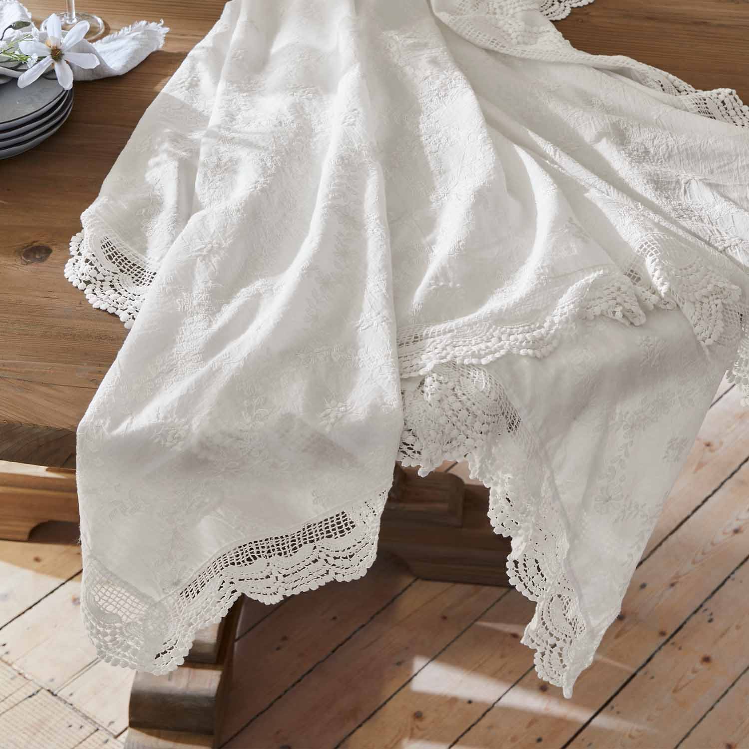 Mantel blanco bordado con borde de encaje sobre mesa de madera, decoración de mesa elegante